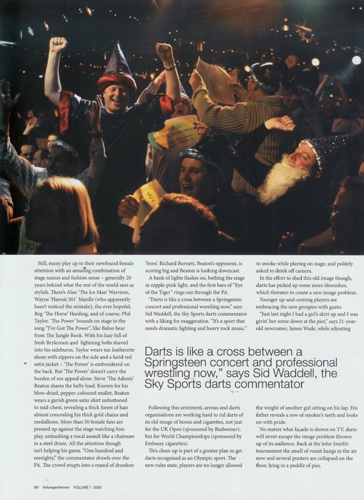 Crowd of fans in costume, including wizard hats, cheering at a darts tournament under bright stage lights.