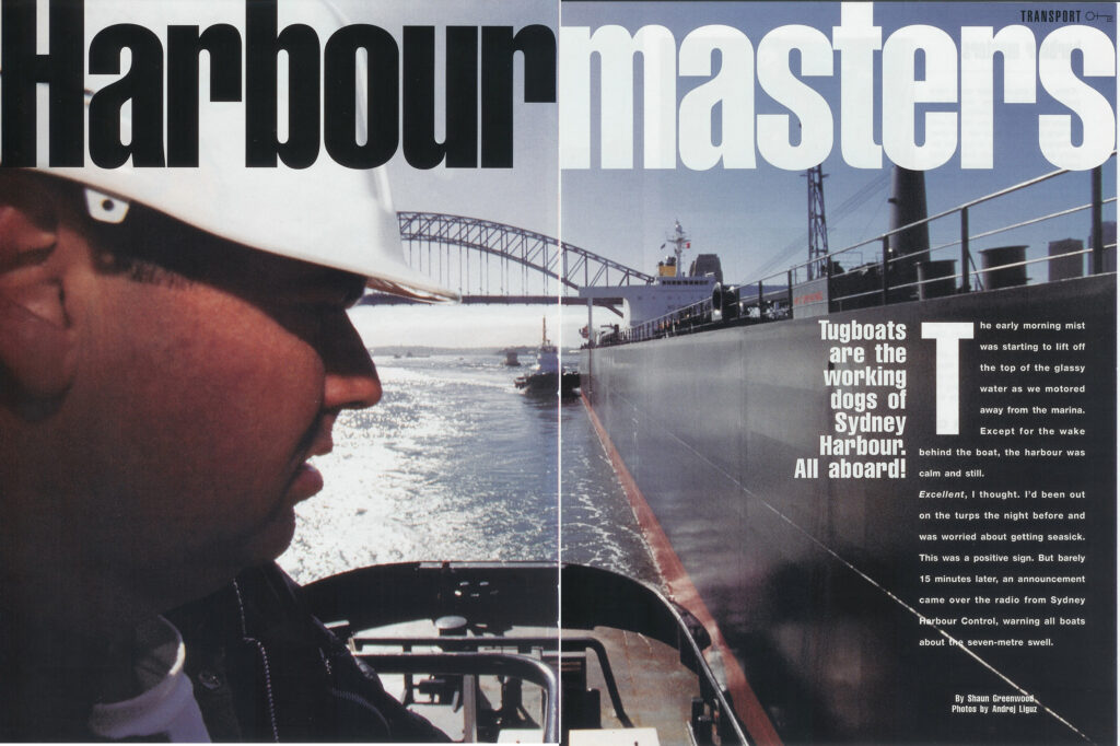 A tugboat crew member in a white hard hat looks out over Sydney Harbour near the Harbor Bridge.