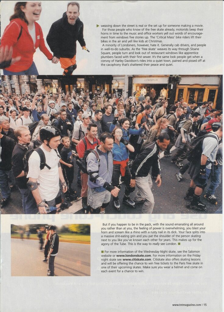 A large crowd of diverse inline skaters filling a city street at night, with buildings and spectators in the background.