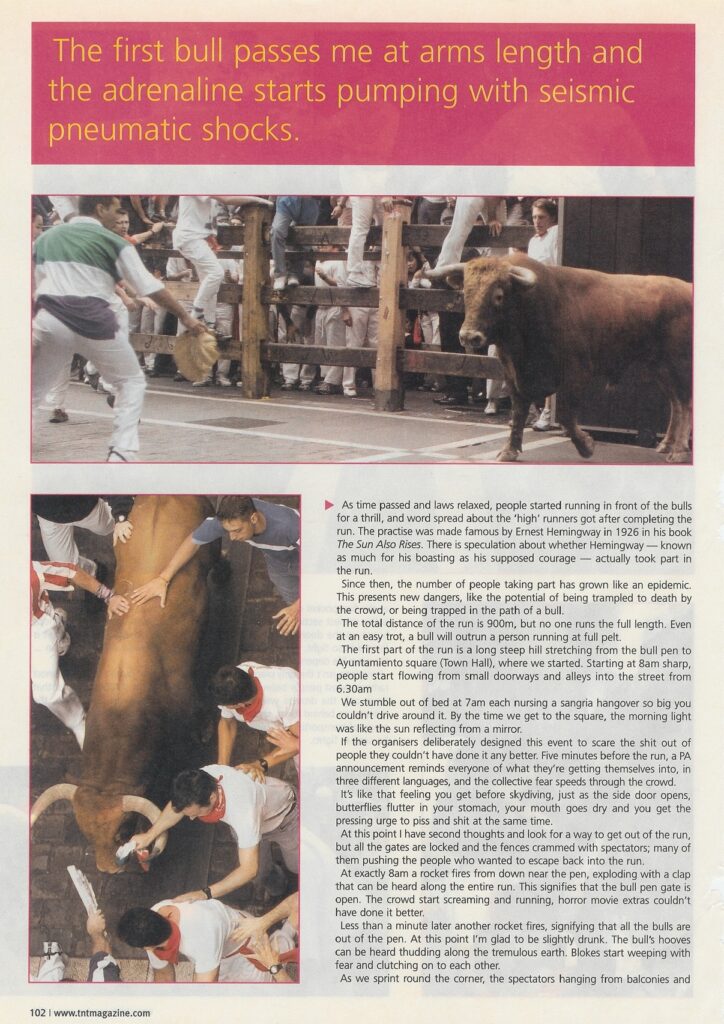 A large brown bull charges through a wooden fence toward runners while others reach down to touch a bull from above.